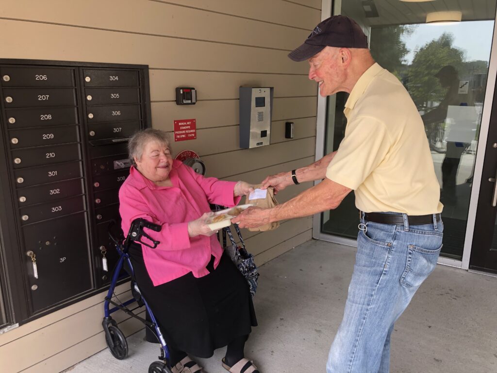 A volunteer hands a meal to a Meals on Wheels participant.