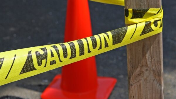 Yellow caution tape tied to wooden post, red cone.